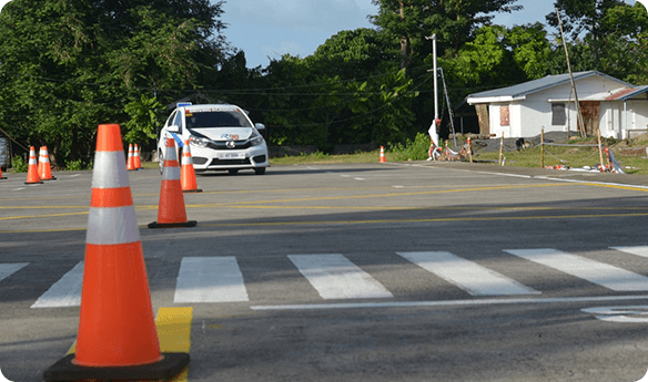 A car driving down the street near orange cones.